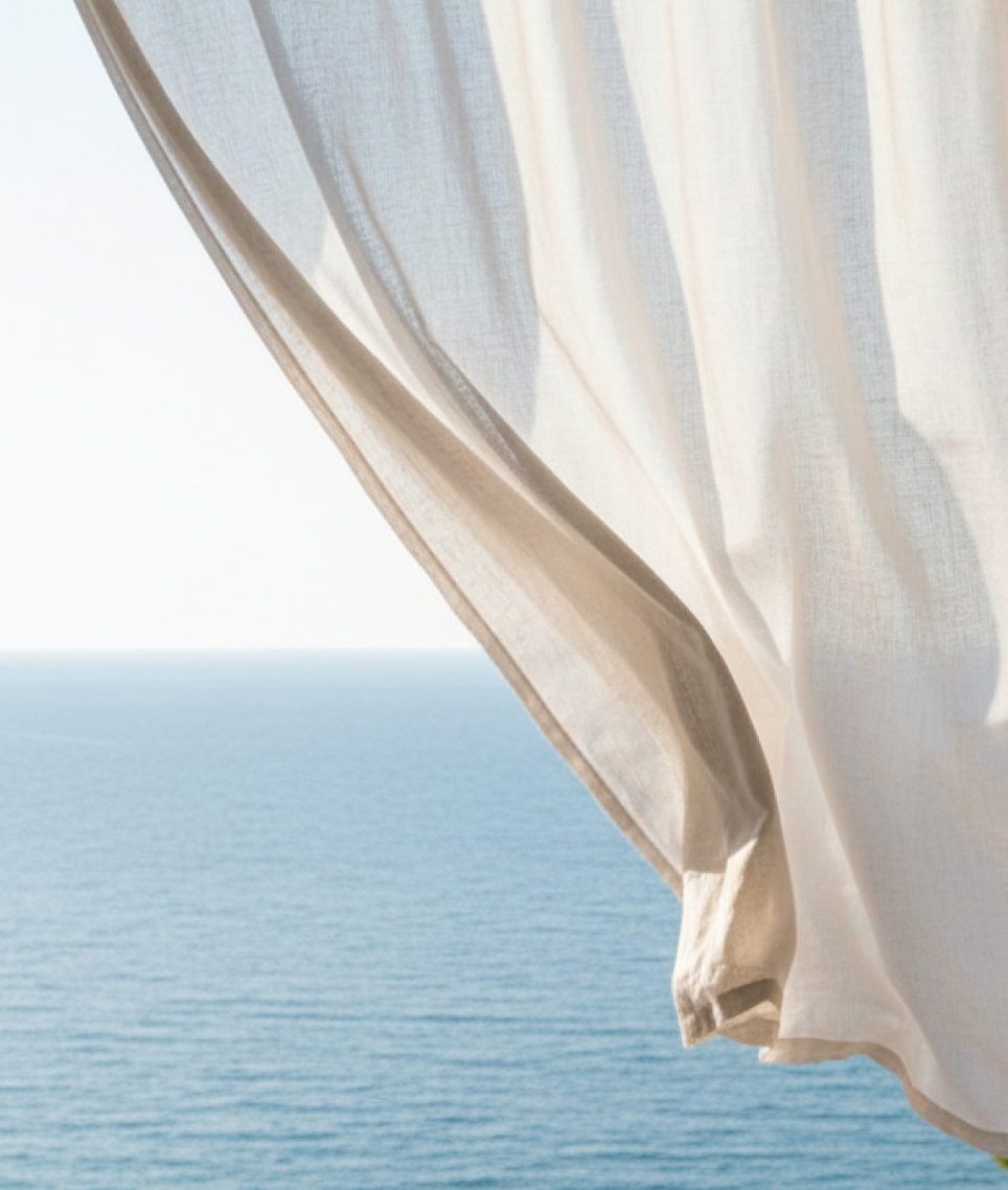 A linen curtain billowing over a window that opens onto the sea