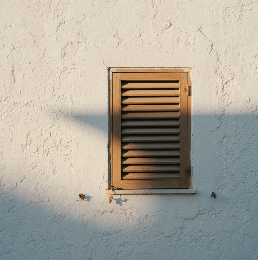 A wooden shutter set into a sunlit whitewashed wall